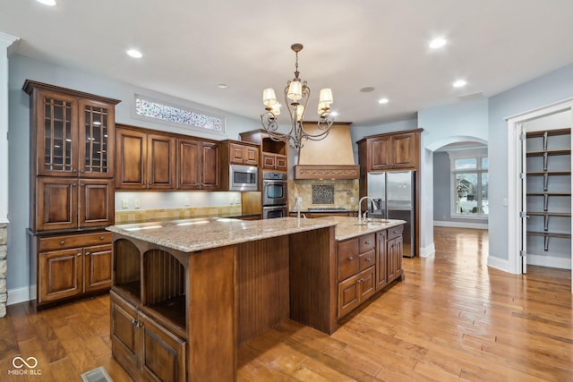 kitchen with a large island, appliances with stainless steel finishes, hanging light fixtures, light stone countertops, and custom exhaust hood