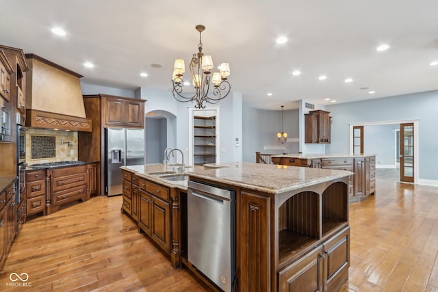 kitchen featuring sink, stainless steel appliances, a spacious island, custom range hood, and decorative light fixtures