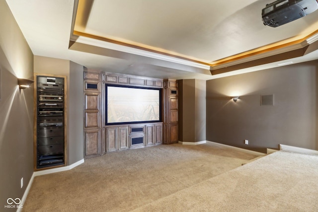 home theater room featuring a raised ceiling, ornamental molding, and light carpet