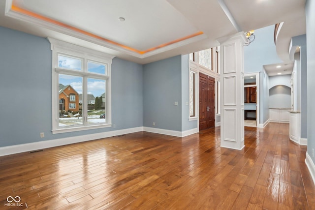 unfurnished living room with hardwood / wood-style flooring, a tray ceiling, and decorative columns