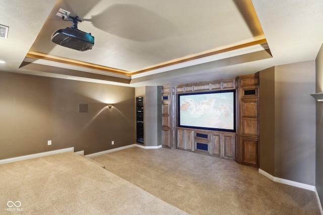 carpeted home theater room with ornamental molding and a tray ceiling