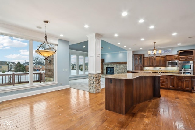 kitchen with hanging light fixtures, appliances with stainless steel finishes, a kitchen breakfast bar, a fireplace, and a kitchen island with sink