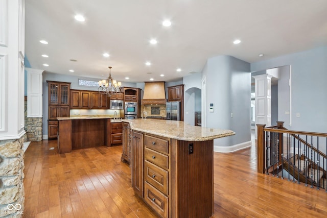 kitchen with stainless steel appliances, wood-type flooring, hanging light fixtures, and a spacious island