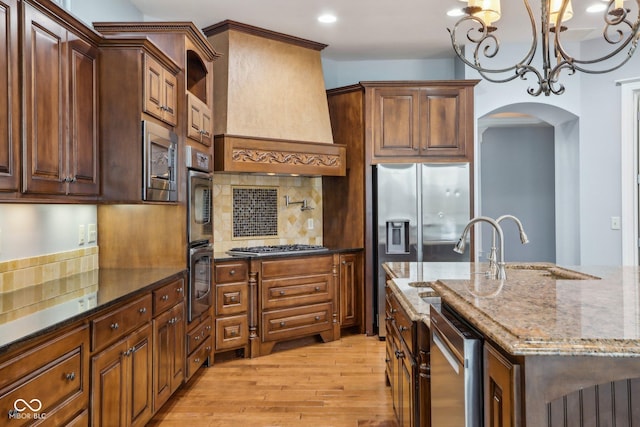 kitchen featuring stainless steel appliances, tasteful backsplash, light hardwood / wood-style floors, custom range hood, and dark stone counters