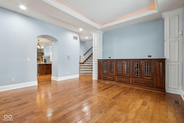 unfurnished room featuring a raised ceiling, ornamental molding, a notable chandelier, and light hardwood / wood-style floors