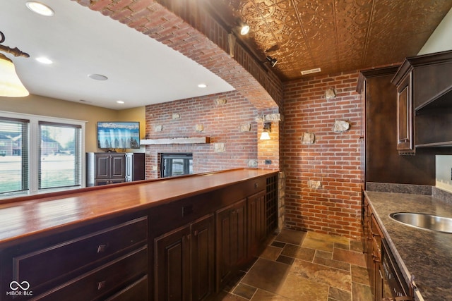 kitchen with dark brown cabinetry, butcher block countertops, sink, and brick wall