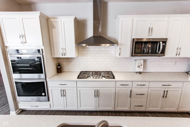 kitchen featuring tasteful backsplash, white cabinets, stainless steel appliances, and wall chimney range hood