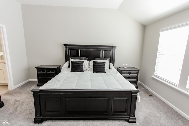 bedroom with light colored carpet, ensuite bathroom, vaulted ceiling, and multiple windows