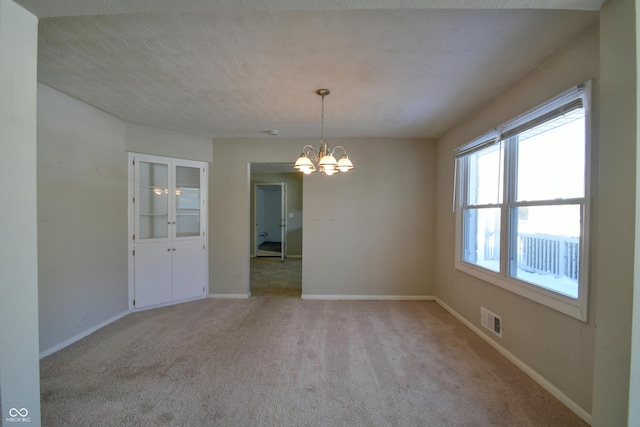 unfurnished room featuring a notable chandelier, light colored carpet, and a textured ceiling