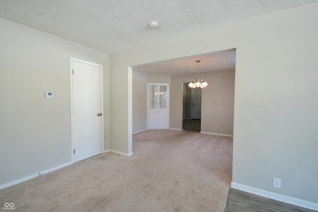 carpeted empty room with a notable chandelier and a textured ceiling