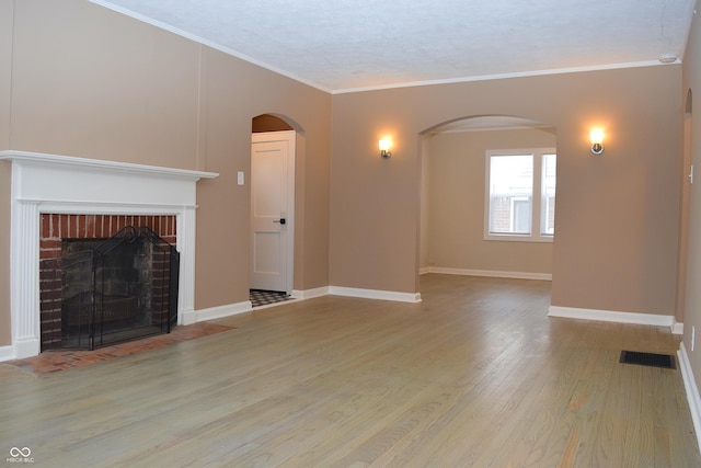 unfurnished living room featuring a brick fireplace, light wood-type flooring, and crown molding