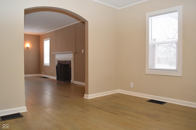 unfurnished living room with a brick fireplace, crown molding, plenty of natural light, and hardwood / wood-style flooring