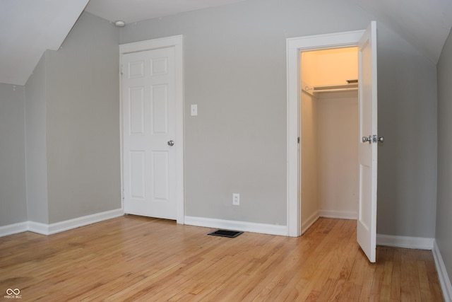 unfurnished bedroom featuring light hardwood / wood-style floors, a walk in closet, a closet, and lofted ceiling