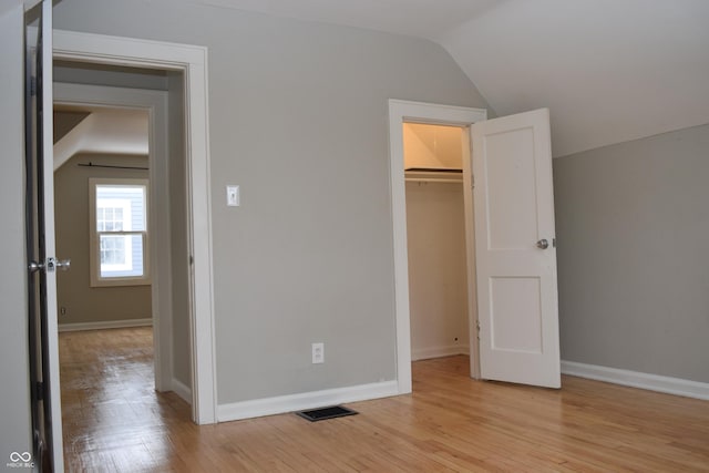 unfurnished bedroom featuring a walk in closet, light wood-type flooring, a closet, and lofted ceiling