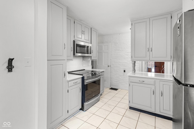 kitchen with light tile patterned flooring, white cabinets, brick wall, and appliances with stainless steel finishes