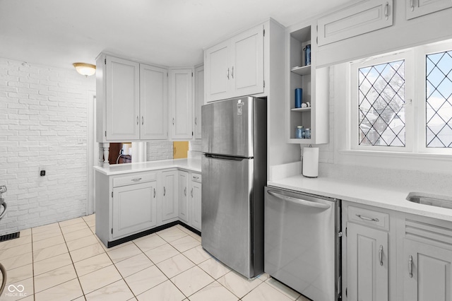 kitchen with light tile patterned floors, stainless steel appliances, white cabinetry, and brick wall