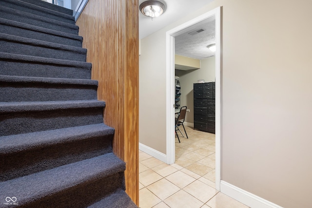 stairway with a textured ceiling and tile patterned floors