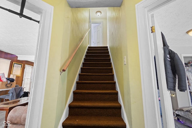 stairway featuring plenty of natural light, wood walls, and a textured ceiling