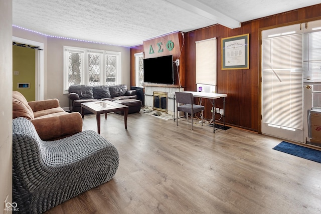 living room with beamed ceiling, light wood-type flooring, a textured ceiling, and wooden walls