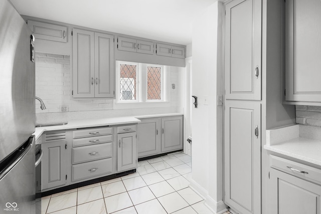 kitchen with tasteful backsplash, gray cabinetry, stainless steel fridge, and sink