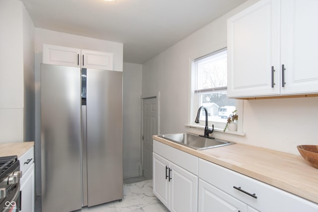 kitchen featuring stainless steel fridge, range with gas cooktop, white cabinetry, and sink