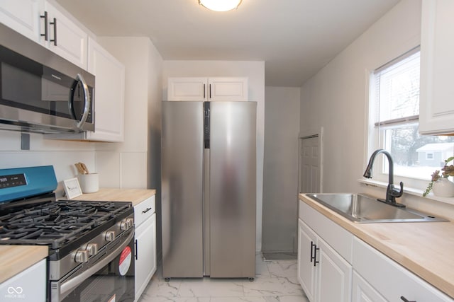 kitchen with butcher block counters, sink, stainless steel appliances, backsplash, and white cabinets