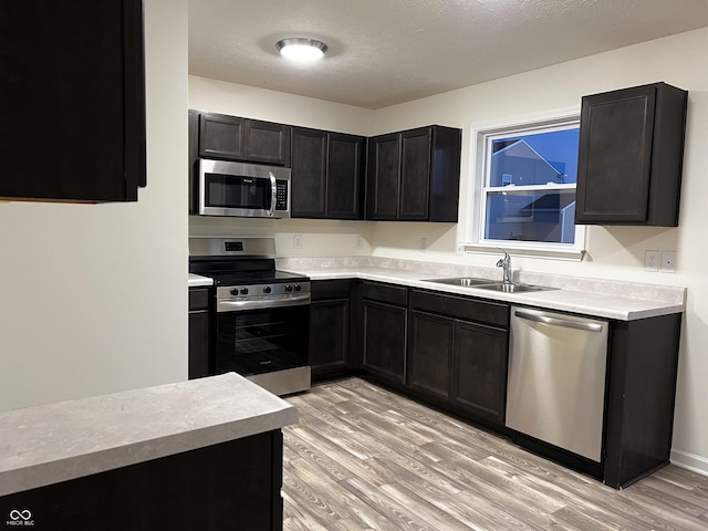 kitchen with light countertops, appliances with stainless steel finishes, a sink, and light wood-style floors