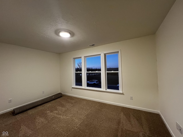 spare room featuring a textured ceiling, dark colored carpet, visible vents, and baseboards