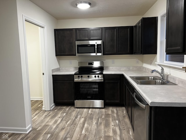 kitchen with light wood-style flooring, a sink, baseboards, light countertops, and appliances with stainless steel finishes