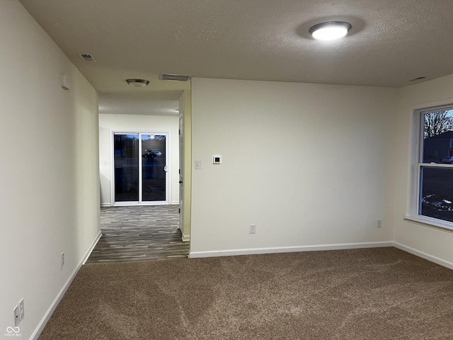 spare room with baseboards, visible vents, dark colored carpet, and a textured ceiling