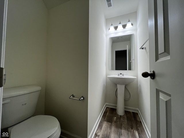 half bathroom with baseboards, visible vents, toilet, and wood finished floors