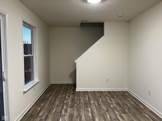 unfurnished room with visible vents, a textured ceiling, baseboards, and dark wood-type flooring