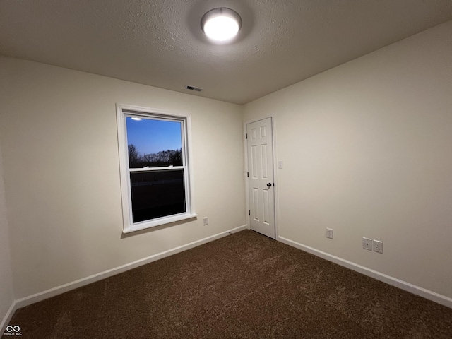 spare room with visible vents, a textured ceiling, dark carpet, and baseboards