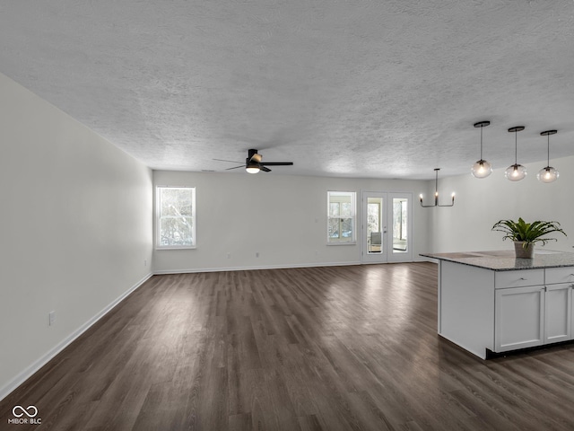 unfurnished living room with dark hardwood / wood-style flooring and ceiling fan with notable chandelier