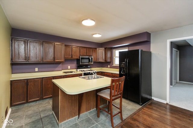 kitchen with a breakfast bar, sink, white range with gas cooktop, black fridge with ice dispenser, and a center island with sink