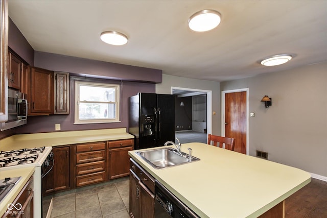 kitchen with a kitchen island with sink, sink, black appliances, and light tile patterned flooring