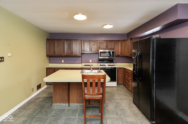 kitchen with sink, white range with gas stovetop, black fridge, light tile patterned floors, and an island with sink