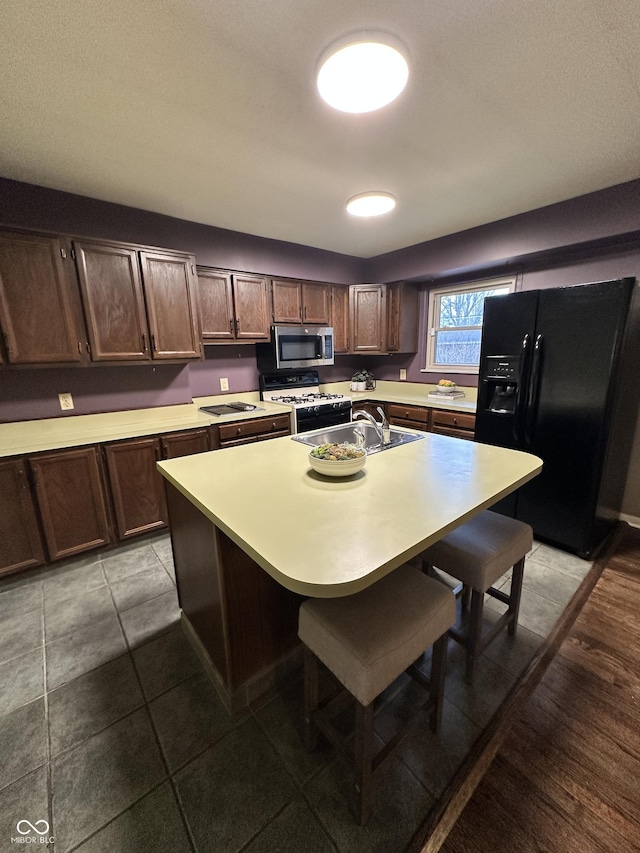 kitchen featuring a kitchen island, range with gas cooktop, a kitchen bar, dark brown cabinetry, and black fridge