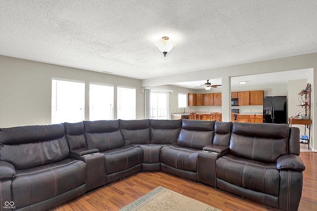 living room featuring a textured ceiling, ceiling fan, and light hardwood / wood-style flooring