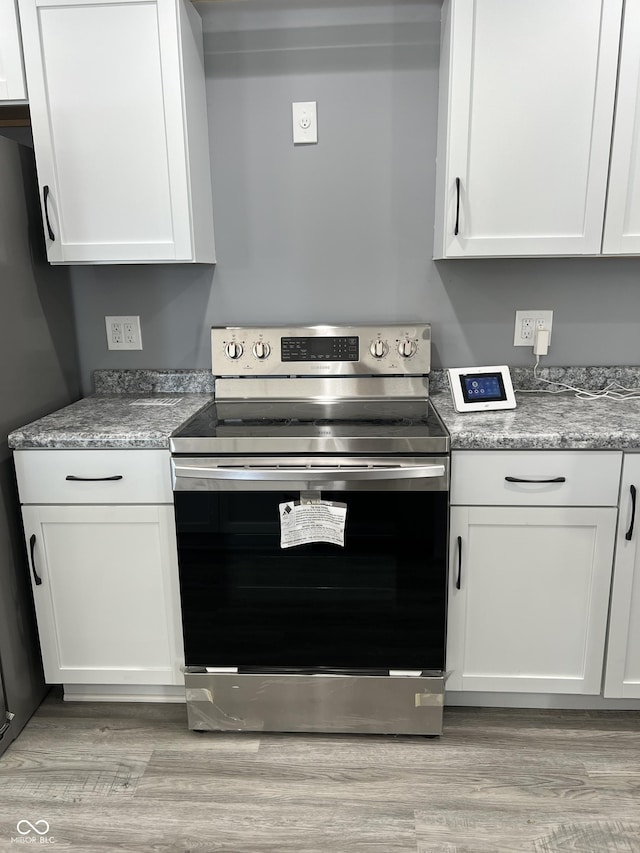 kitchen with white cabinets, light hardwood / wood-style floors, stainless steel electric stove, and black refrigerator