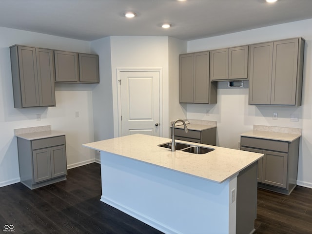 kitchen featuring an island with sink, gray cabinetry, dark hardwood / wood-style flooring, light stone countertops, and sink