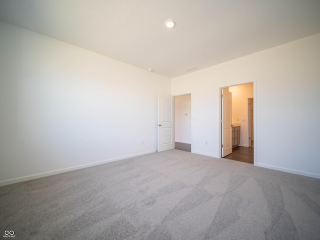 unfurnished bedroom featuring ensuite bath, baseboards, and dark carpet