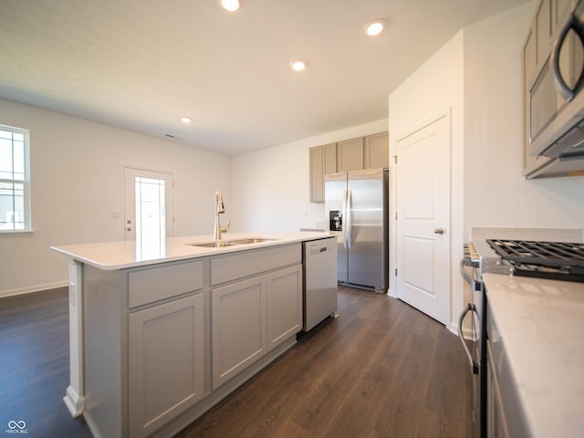 kitchen featuring a sink, gray cabinetry, a center island with sink, stainless steel appliances, and dark wood-style flooring