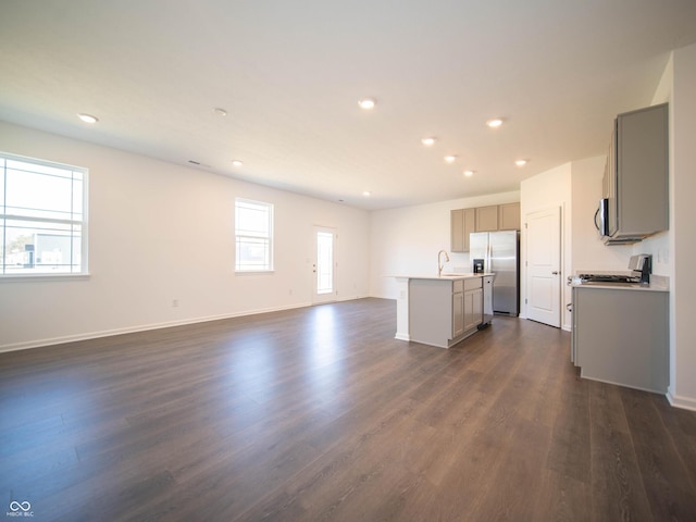 interior space with open floor plan, a center island with sink, gray cabinets, stainless steel appliances, and a sink