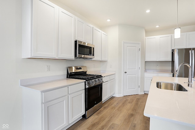 kitchen featuring appliances with stainless steel finishes, white cabinetry, sink, light wood-type flooring, and pendant lighting