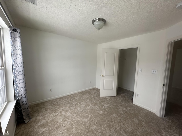 unfurnished bedroom with a textured ceiling, a closet, carpet, and a spacious closet