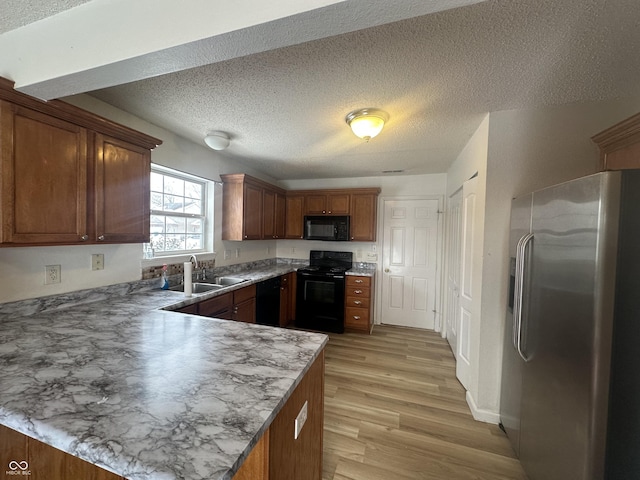 kitchen featuring kitchen peninsula, a textured ceiling, black appliances, light wood-type flooring, and sink