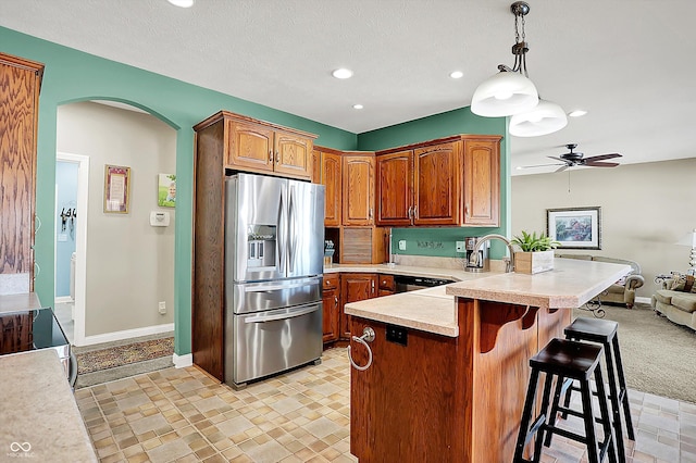 kitchen with pendant lighting, stainless steel refrigerator with ice dispenser, light colored carpet, ceiling fan, and a kitchen breakfast bar