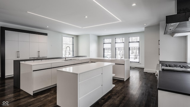 kitchen featuring kitchen peninsula, dark hardwood / wood-style floors, a kitchen island, white cabinets, and sink