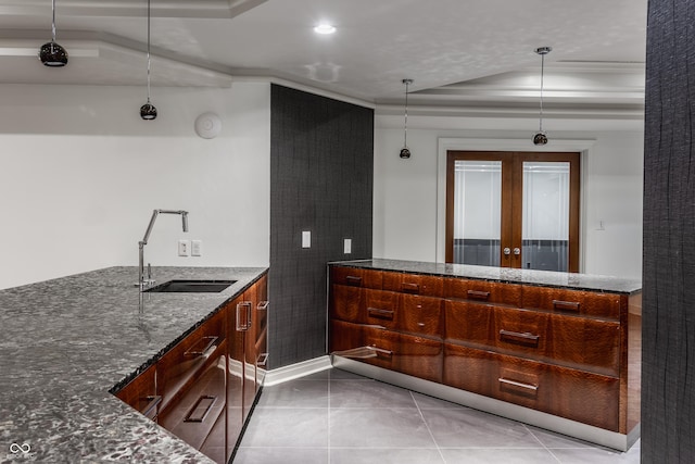 kitchen with dark stone countertops, pendant lighting, a raised ceiling, sink, and ornamental molding